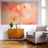 Bright pink, orange, and yellow abstract painting hangs on a white wall above a media stand in living room, next to a cozy chair.