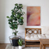 Purple, pink, and orange abstract painting hangs above a wooden bench, next to a large green plant.