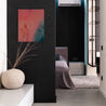 An abstract painting made with pink, purple, blue, and green washes of acrylic paint hangs on a black wall in a sleek home or hotel room.