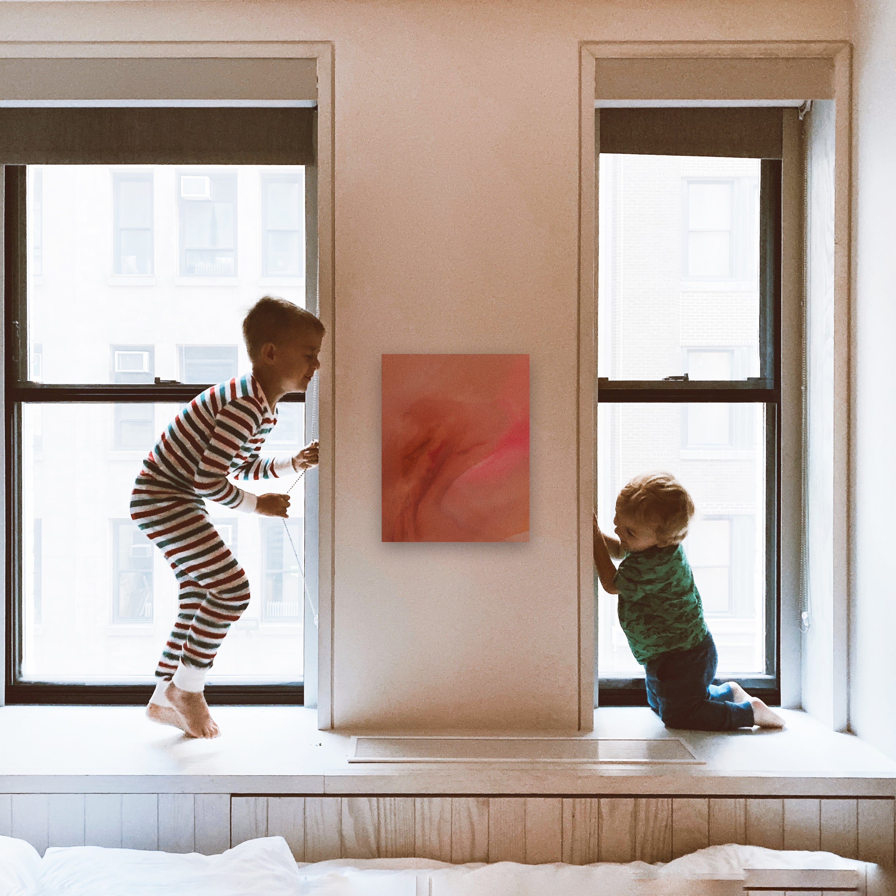 Small pink and orange abstract painting hangs on a wall between two children playing.